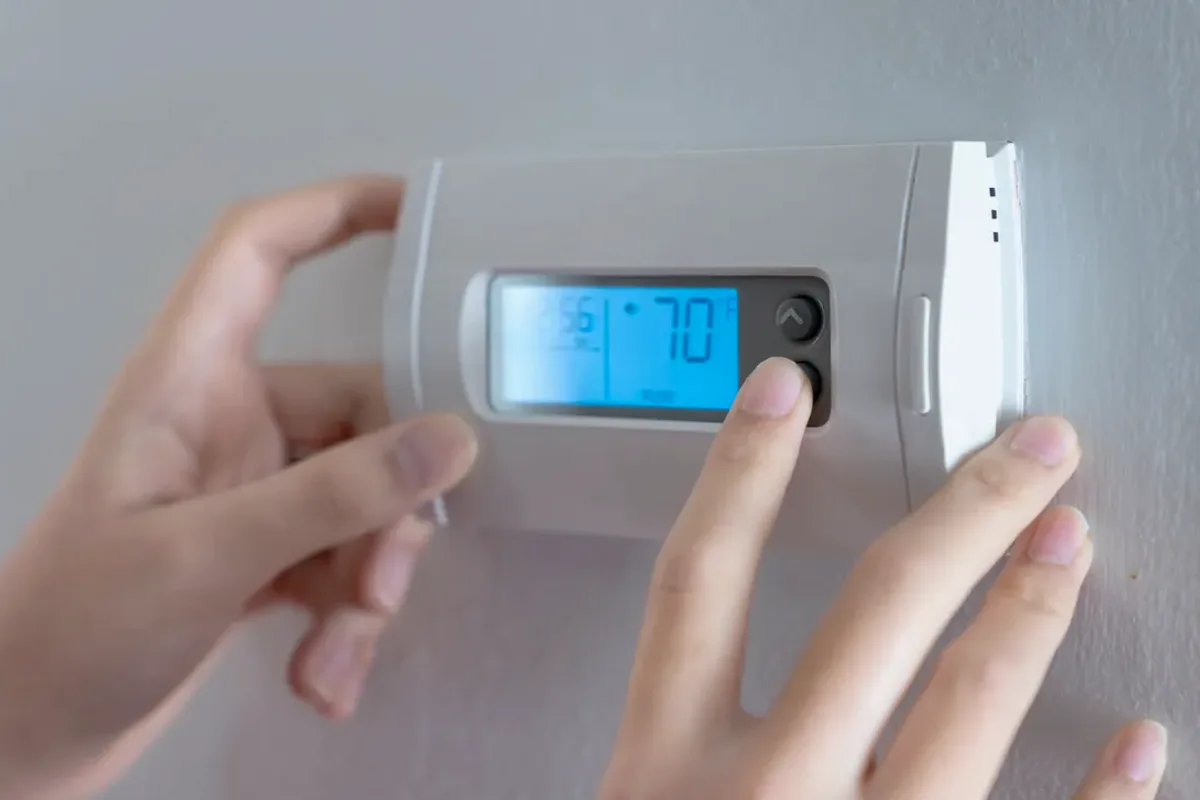 Hands adjusting a digital wall thermostat